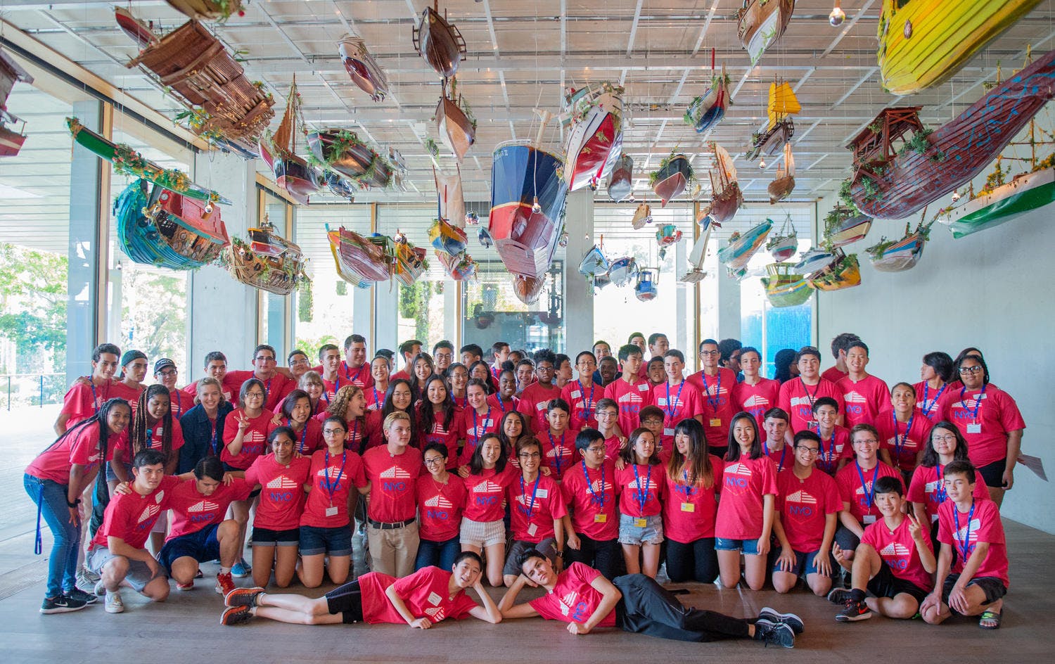 Musicians of NYO2 pose in an art museum with various ships and boats hanging overhead