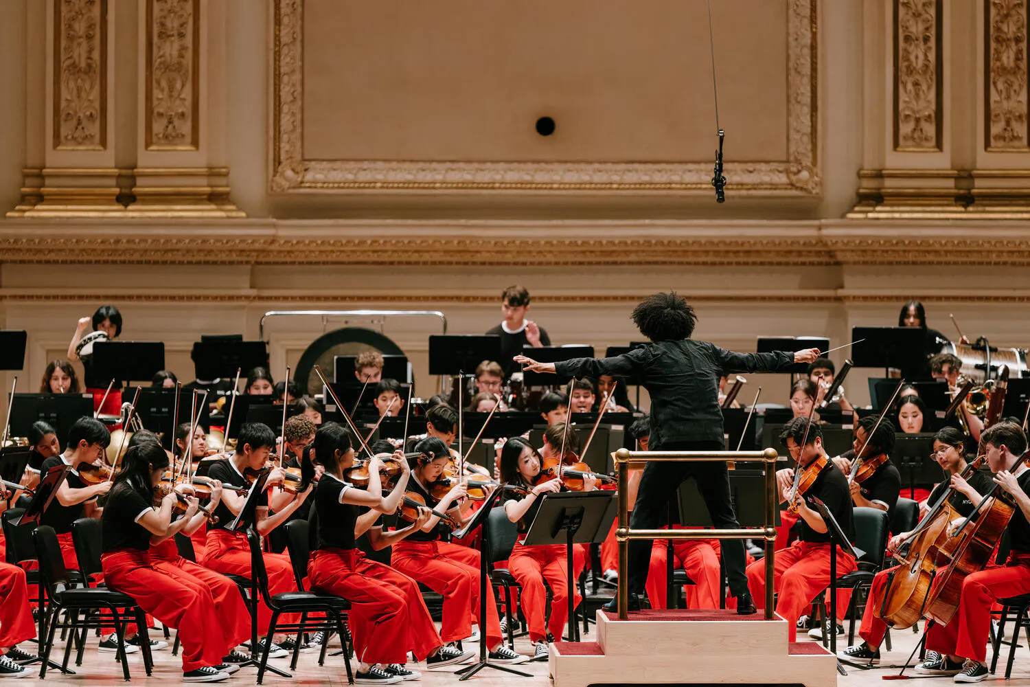 The NYO2 Orchestra performs on stage at Carnegie Hall as the conductor leads them, arms outstretched
