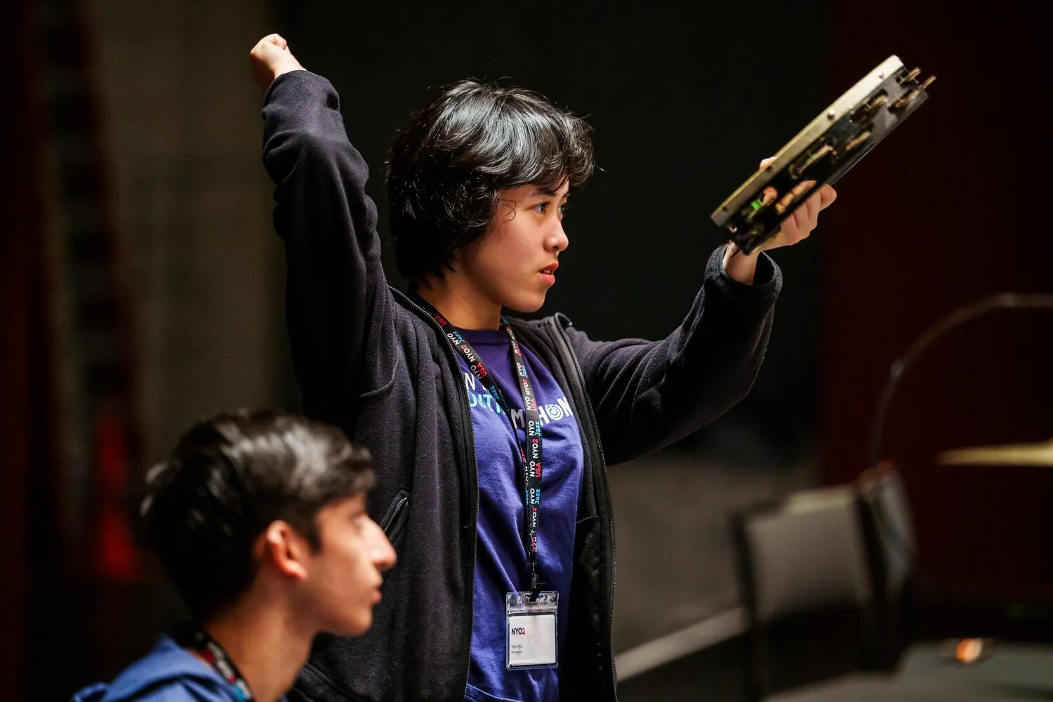 A female NYO2 musician holds out a tambourine, hand lifted to strike it