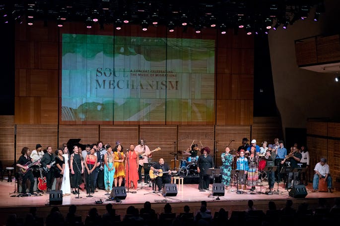 A group of singers perform with a band in Zankel Hall; a "Soul Mechanism" projection is on the wall.