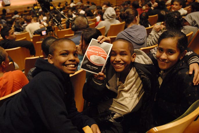Three children seated in Zankel Hall hold up a Playbill for Perelman American Roots.