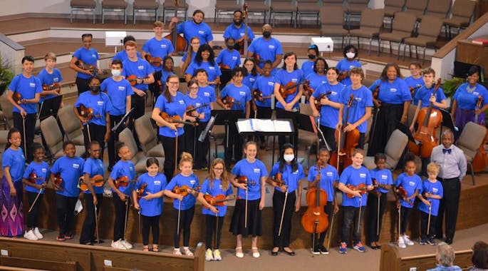 Looking from above, a group of musicians and faculty in blue shirts pose and hold their instruments.