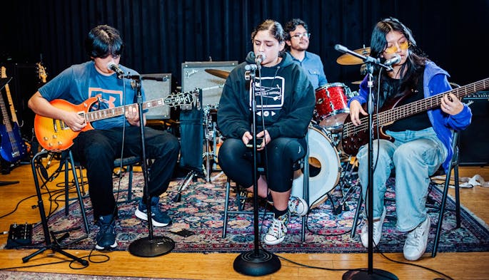 Four teenagers in street clothes, seated, play together in a band.