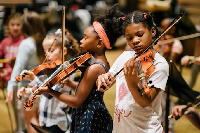 A group of young girls practice playing violin