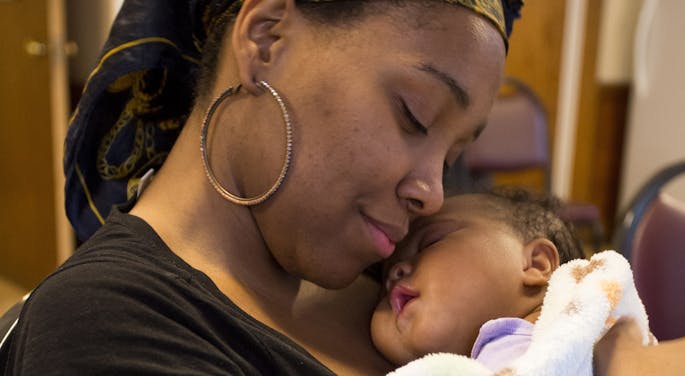 A young woman wearing a head scarf cuddles a sleeping baby
