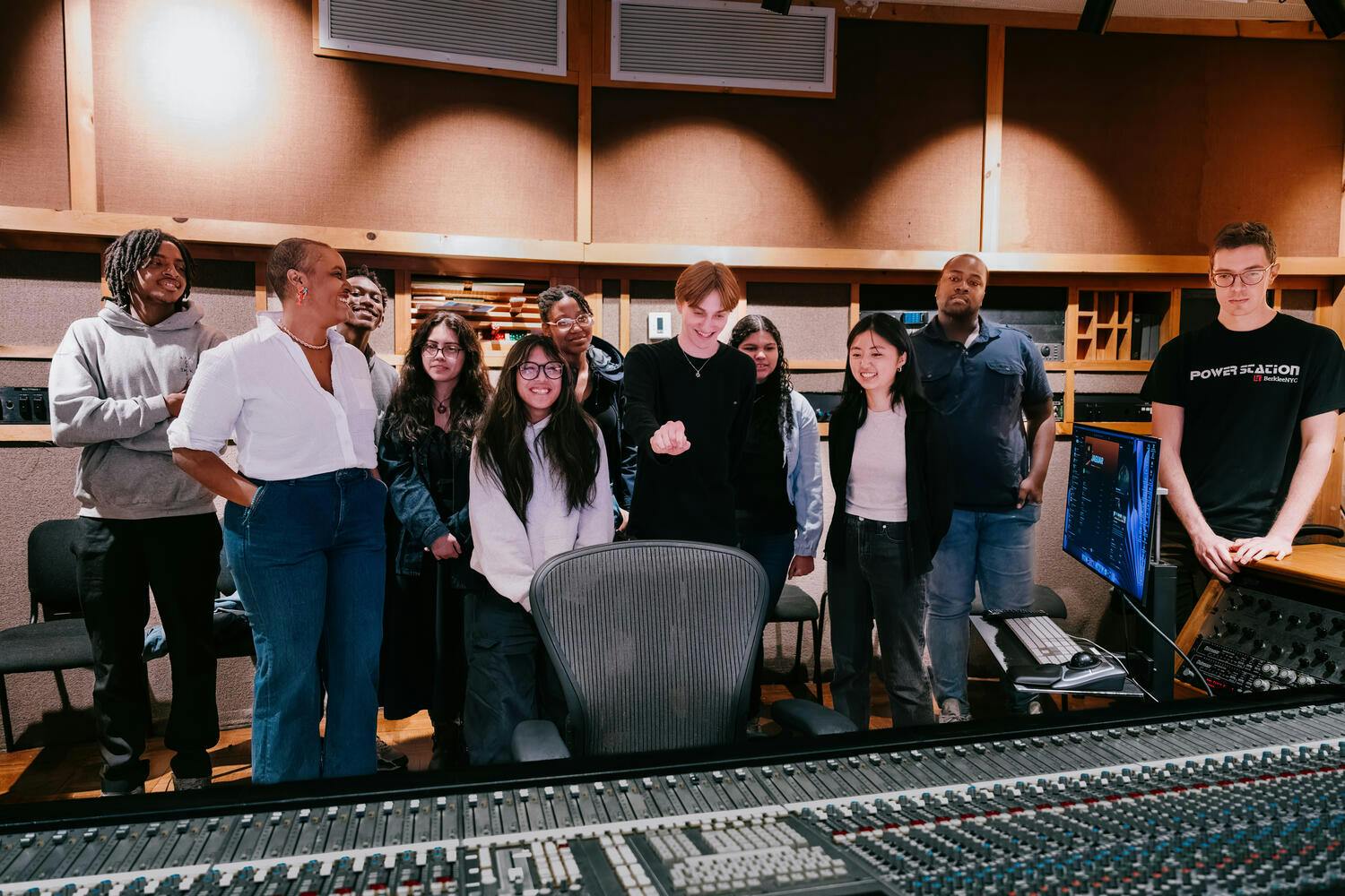 The B-Side participants gather together before a mixing board in a recording studio
