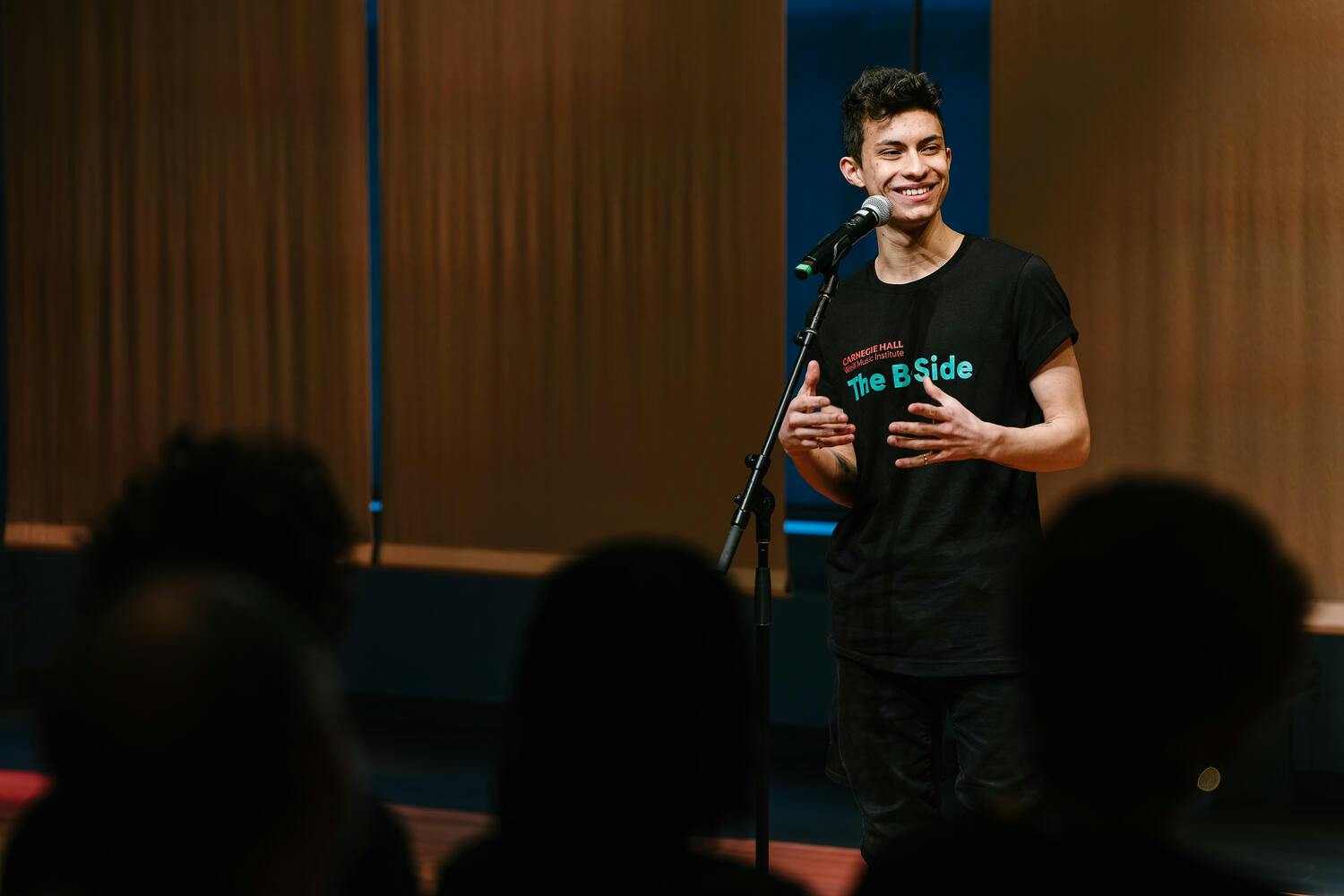 A smiling young man speaks into a microphone before an audience