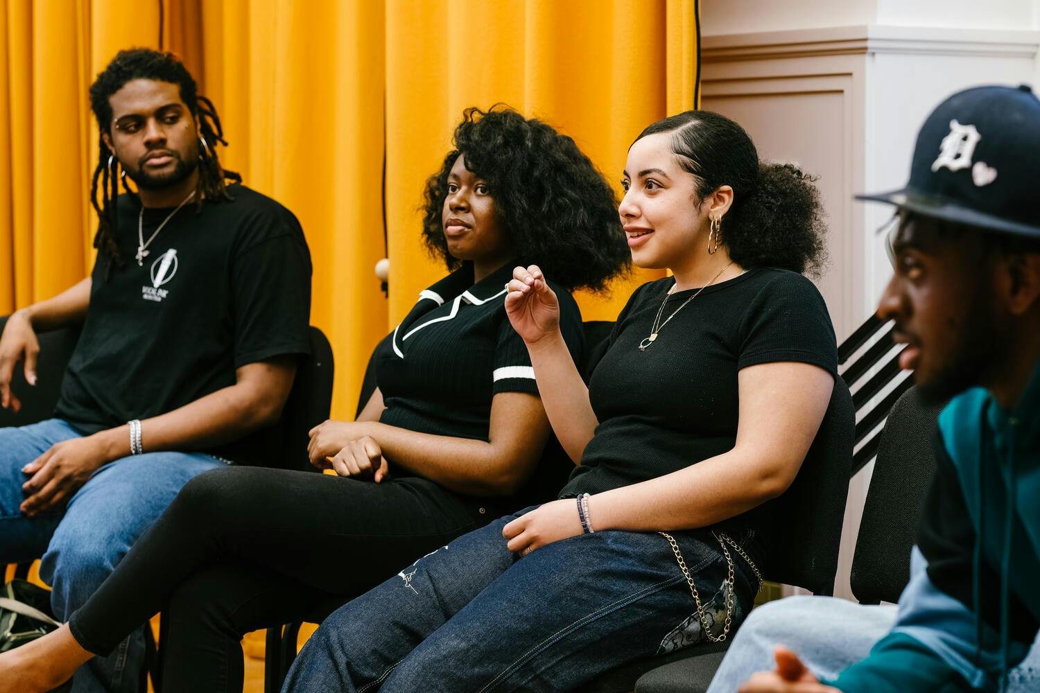 A smiling young woman sits, hand upraised, as three other B-Side participants look on