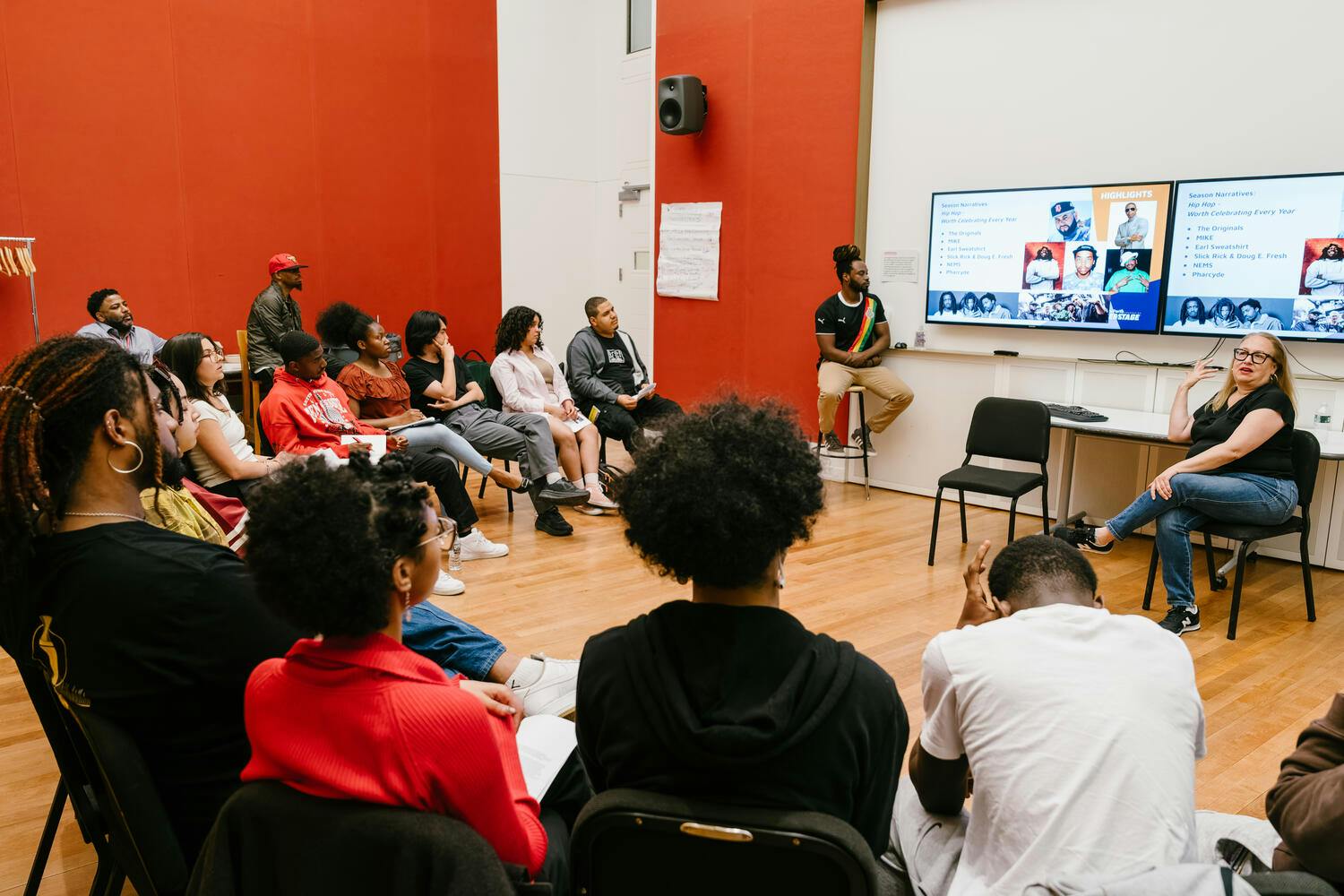 A woman teaches a group of young men and women seated in a semi-circle