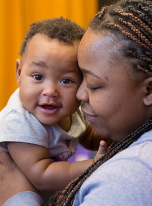 A woman with braided hair holds a smiling baby.