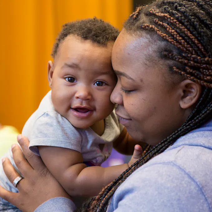 A woman with braided hair holds a smiling baby.