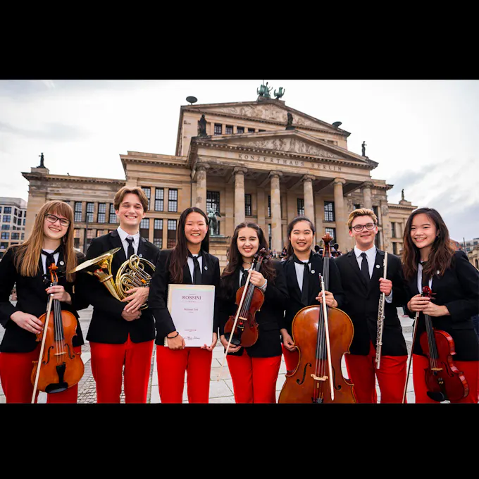 Young musicians in black blazers and red pants stand holding their instruments outside the concert hall in Berlin