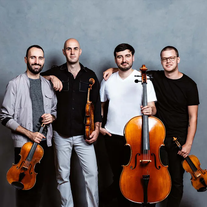 The members of the string quartet "Invoke" hold their instruments in front of a blue wall.