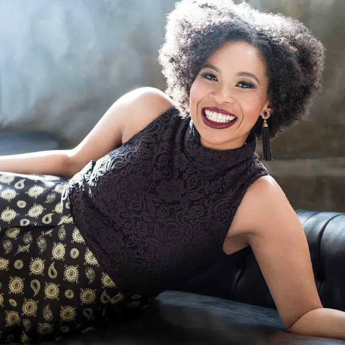 A smiling Golda Schultz reclines on a black sofa