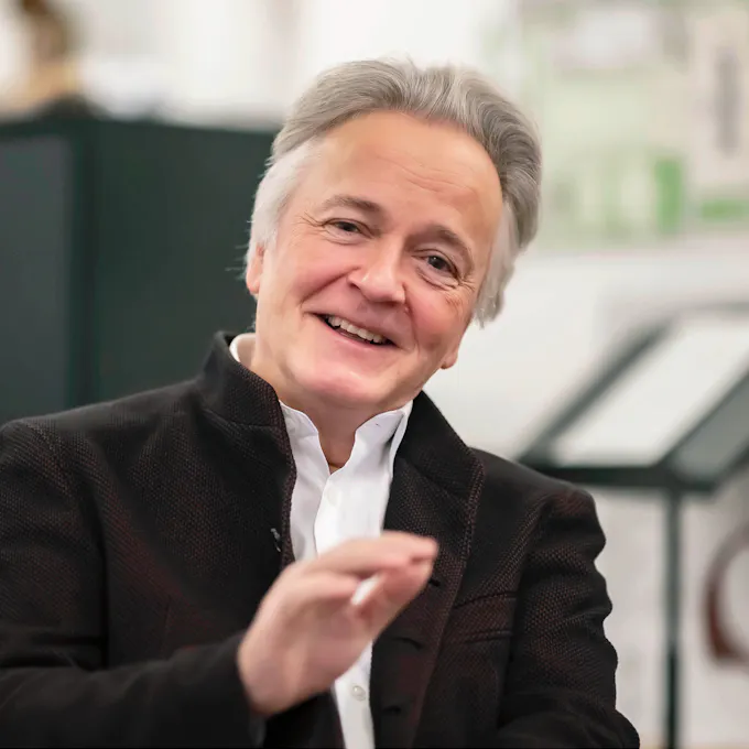 Hartmut Höll smiles in front of a music stand