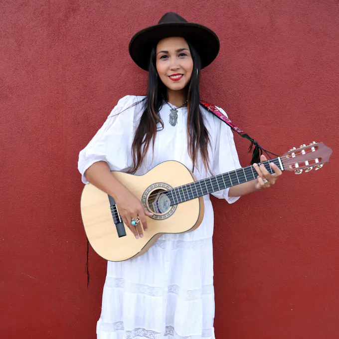 Sonia De Los Santos wearing a white dress with her guitar
