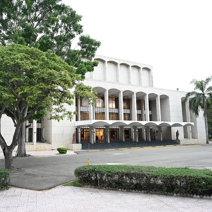 A white stone auditorium with tall windows flanked by trees