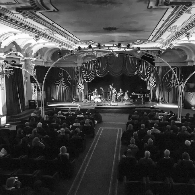 Black and white photo of an audience watching a band perform on a curtained stage
