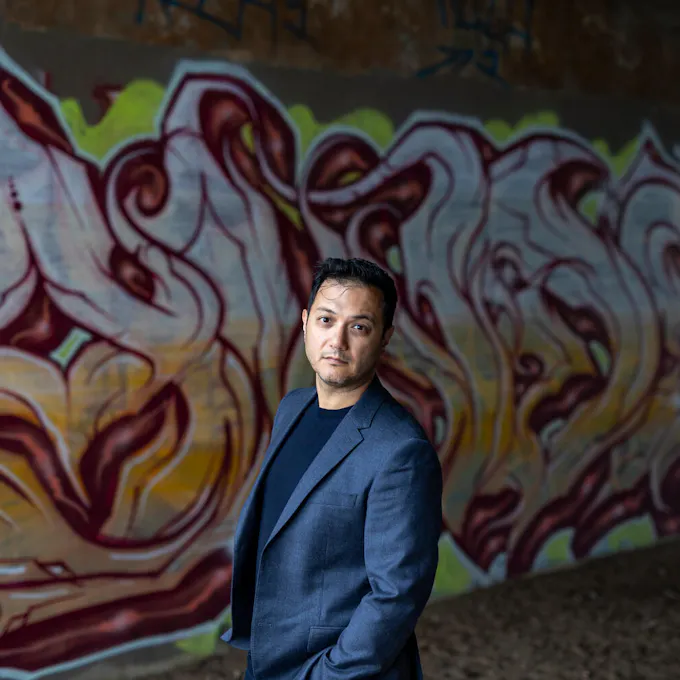 Nicholas Phan stands in front of a wall painted with a flower mural