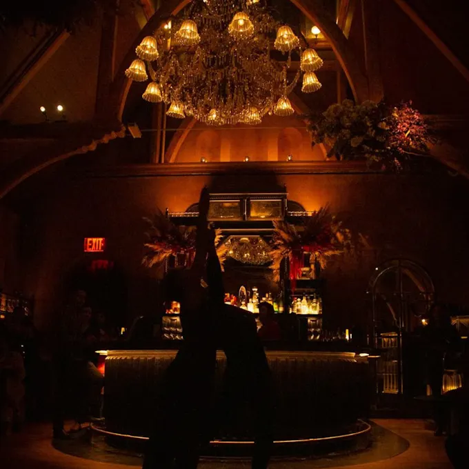 A chandelier hangs over the bar of a cocktail lounge in evening lighting