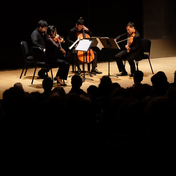 A string quartet performs on a spotlighted stage as an audience watches