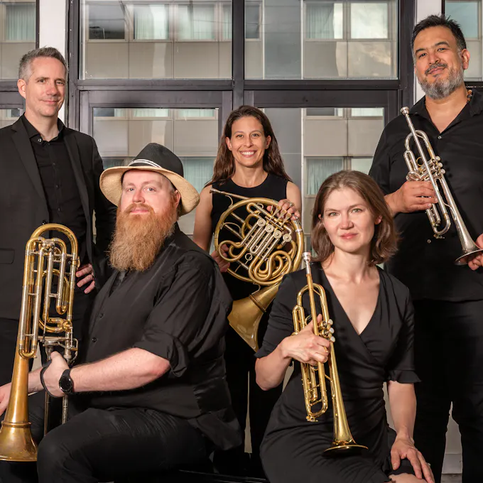 Members of Gotham City Brass Quintet sitting and standing in front of a window