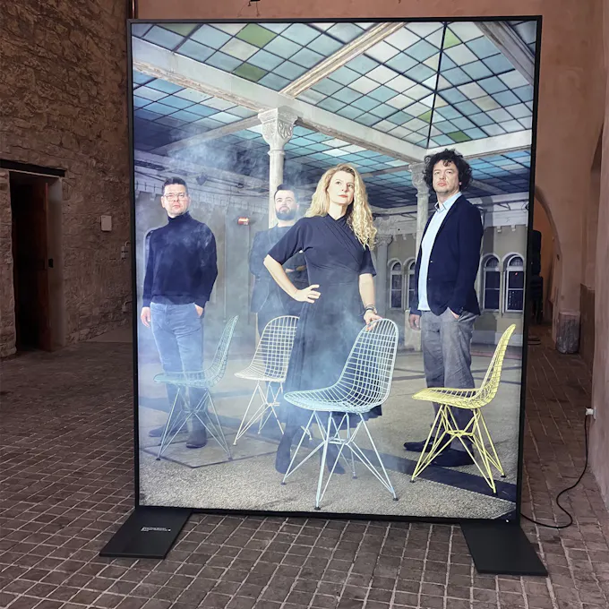 Four people standing in front of chairs, within a rectangular digital screen