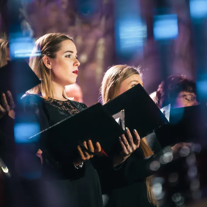 Three young women in a choir sing, holding song books