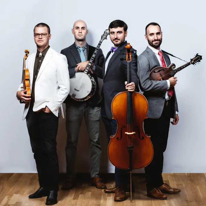 Four young male musicians wearing suits and ties pose together with their instruments
