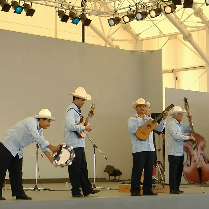 Four male musicians wearing blue shirts and cowboy hats perform on stage
