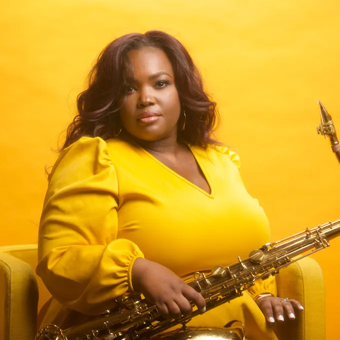Camille Thurman sitting and holding a tenor saxophone