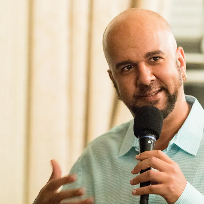 A bearded smiling young man speaks into a microphone
