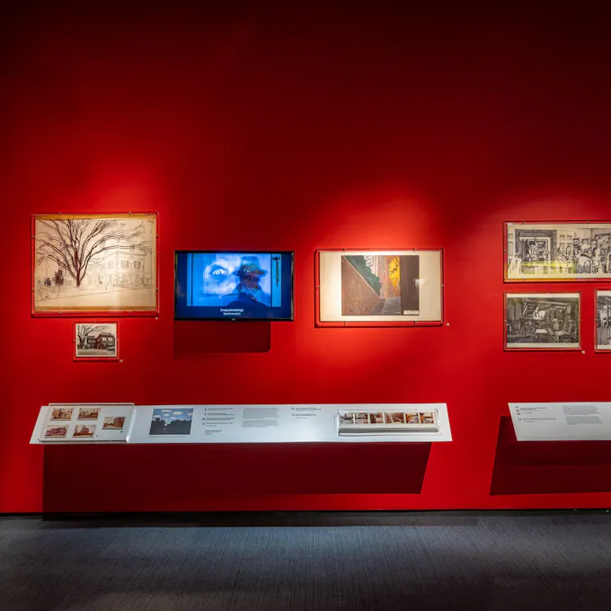 Multiple paintings on the orange wall of a museum exhibit