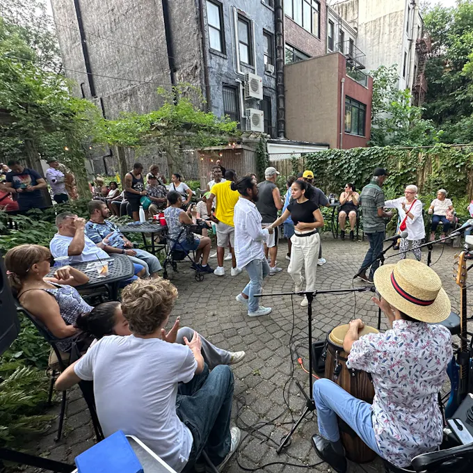 Men and women dance together in a courtyard lined by buildings and trees