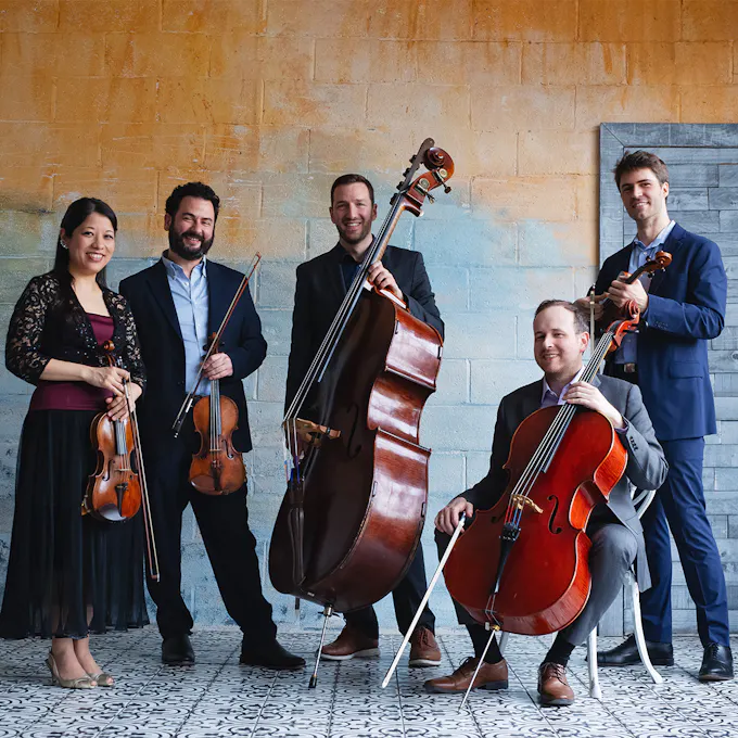 Members of Toomai String Quintet sitting and standing while holding string instruments