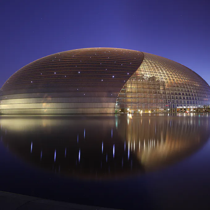 A round, gold metallic concert hall lit up overlooking a lake