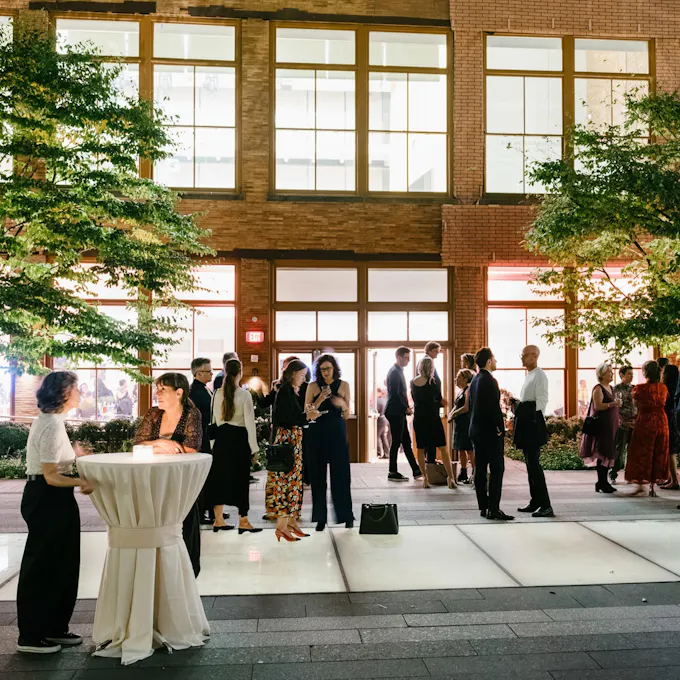 People mingle on a lighted terrace flanked by trees