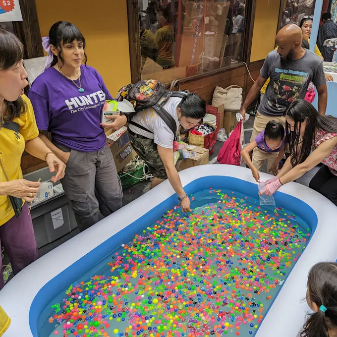 People dunking plastic bags into a kiddie pool filled with colorful plastic balls