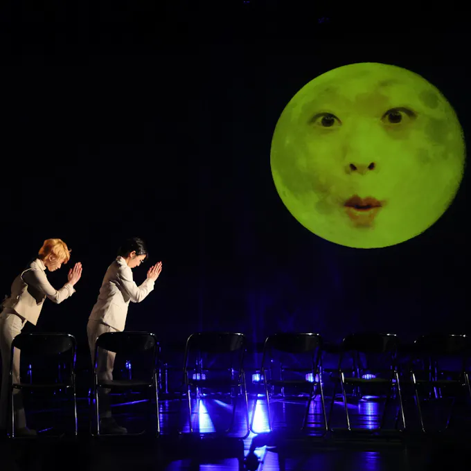 Two Japanese women bow to a green moon with a human face
