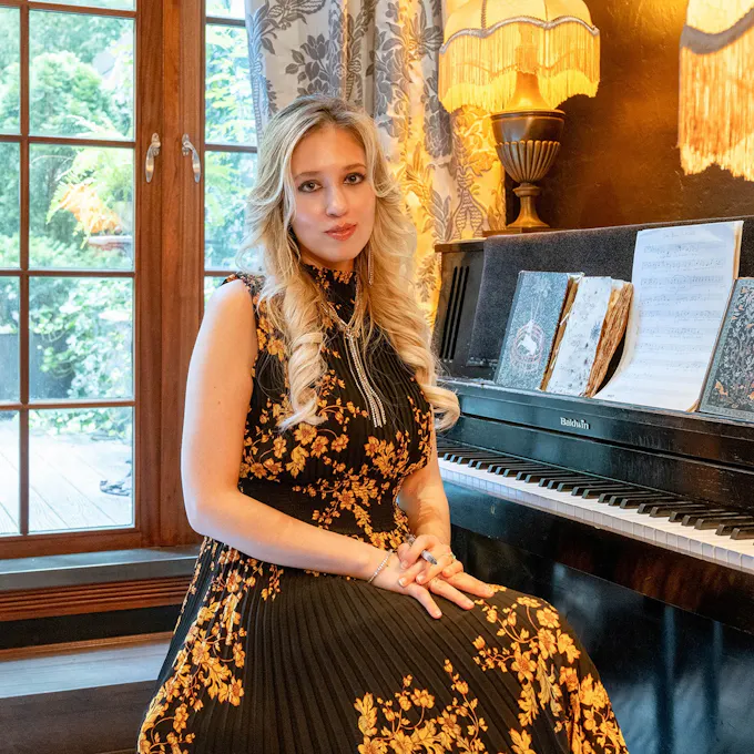 Stephanie Susberichs sits at a piano before a window