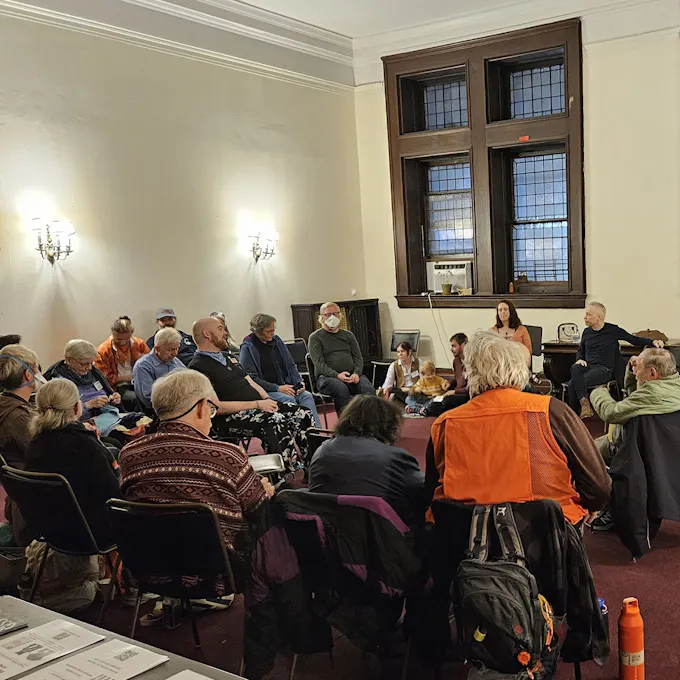 A group of people sit in a room with candelabras on the wall