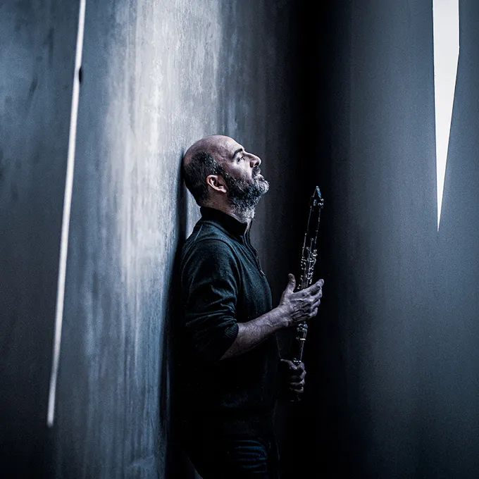 Kinan Azmeh leans against a wall holding his clarinet