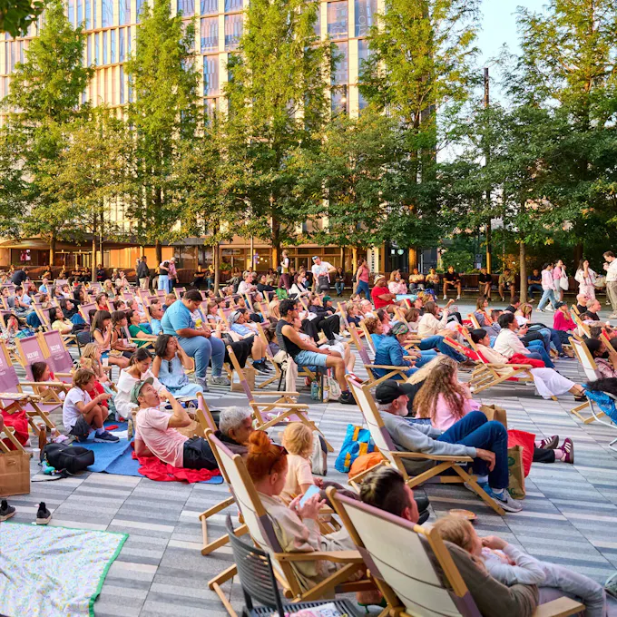 People lounge on blankets and in deck chairs in a city park