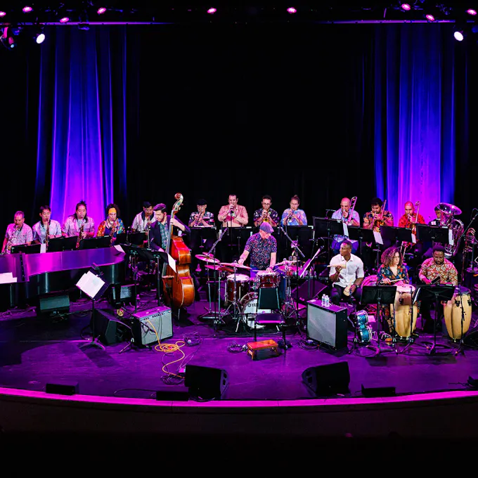 A band performs on stage with blue curtains and purple lighting