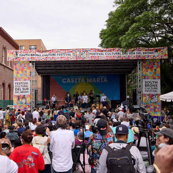 An audience watches a band play on an outdoor stage backed with a banner titled "Casita Maria"