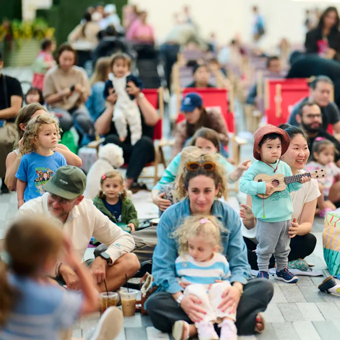 Parents sit with their toddlers outdoors on blankets and in deck chairs
