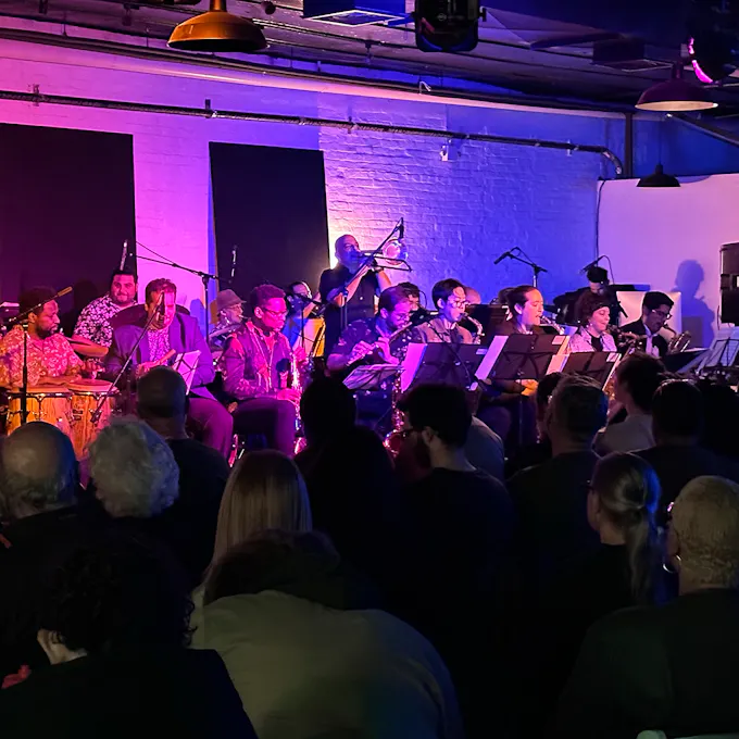 A band performs in a small brick-walled room as an audience watches