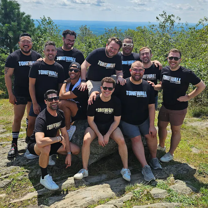 The men of TONEWALL pose together outdoors wearing black "TONEWALL" t-shirts