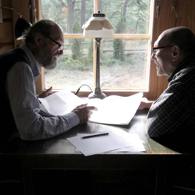 Arvo Pärt and another person sitting at a table in front of a window