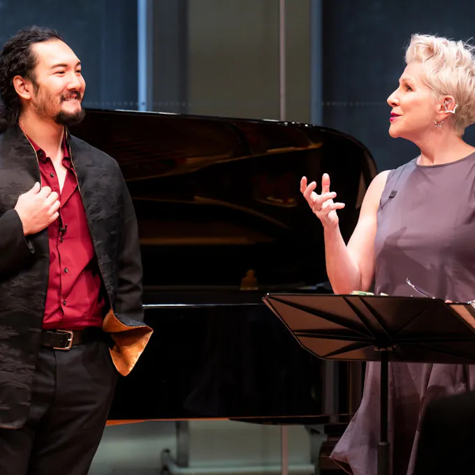 Joyce DiDonato speaks to a smiling young man as they stand on stage before a grand piano